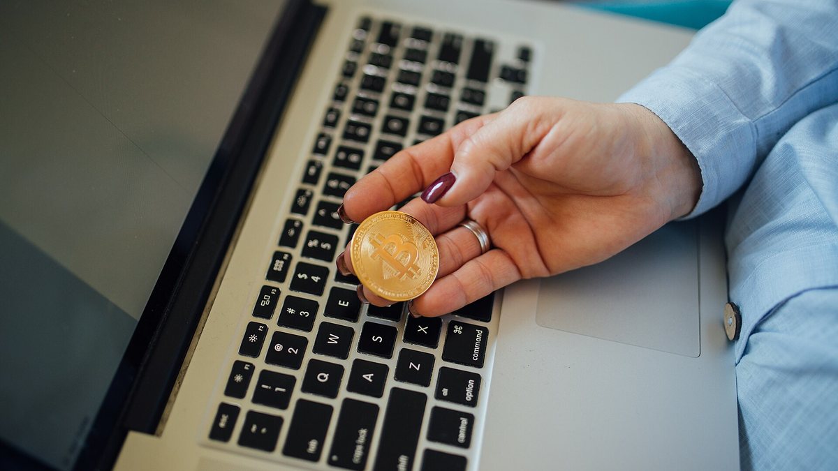 Hand holding a gold Bitcoin coin above a laptop keyboard