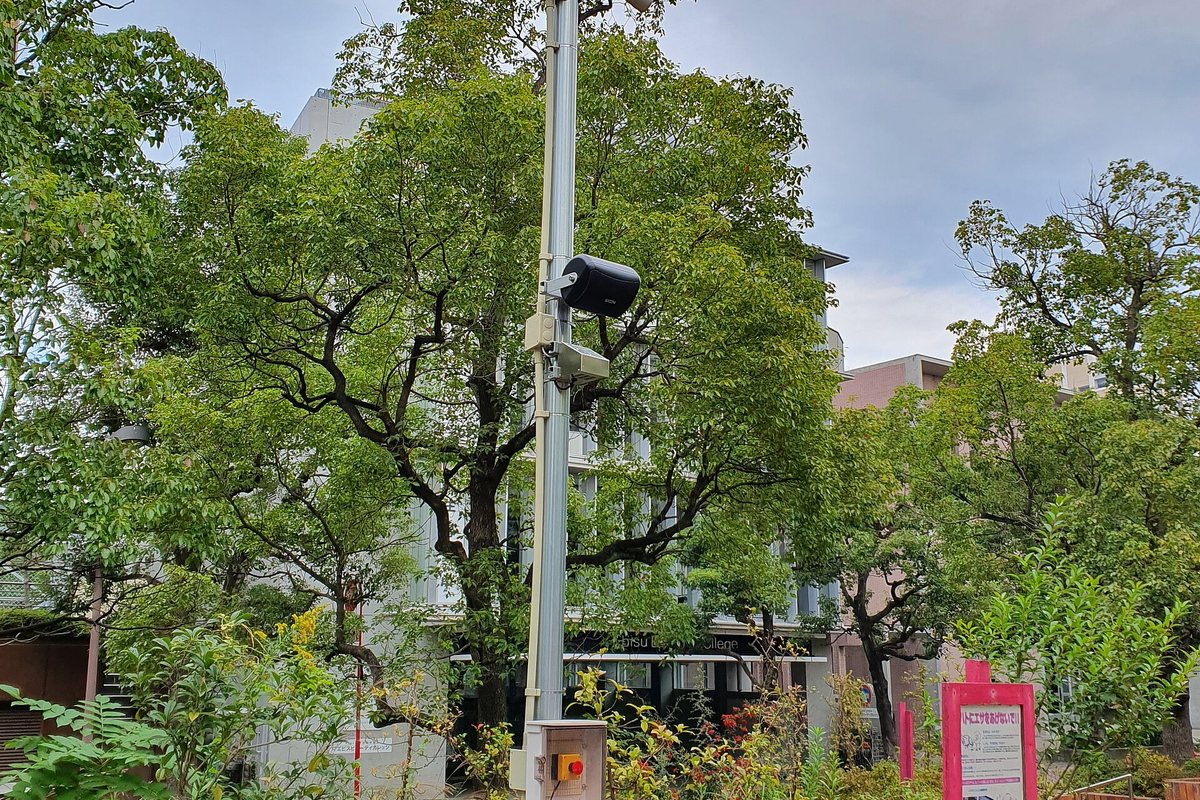 Street pole with a surveillance camera among trees